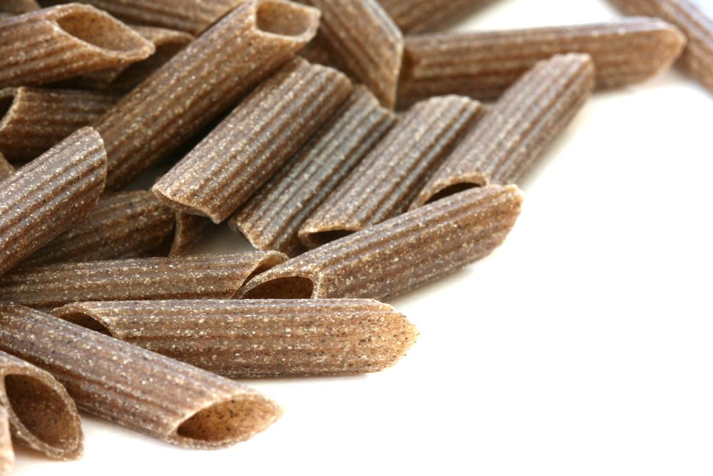 Raw wholegrain pasta scattered on white background